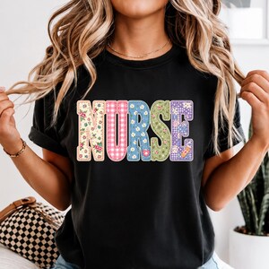 Könnte beinhalten: Ein schwarzes T-Shirt mit kurzen Ärmeln und dem Wort NURSE in großen Blockbuchstaben. Jeder Buchstabe hat ein einzigartiges Muster, darunter Blumenmuster, rosa-weißes Vichy-Karo, blaue Gänseblümchen und eine kleine orangefarbene Pflastergrafik.