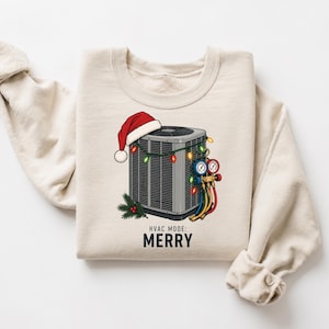 May include: A beige crewneck sweatshirt featuring a graphic of a gray HVAC condenser unit wearing a red Santa hat. The unit is decorated with colorful Christmas lights, a pine sprig, and a manifold gauge set. The text reads HVAC MODE: MERRY.