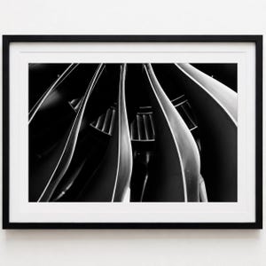 Puede incluir: Impresión artística enmarcada en blanco y negro que presenta una composición abstracta de formas curvas en forma de cuchilla. La imagen tiene un alto contraste, con sombras y luces fuertes, creando un efecto dramático. La obra de arte está montada en un marco negro.