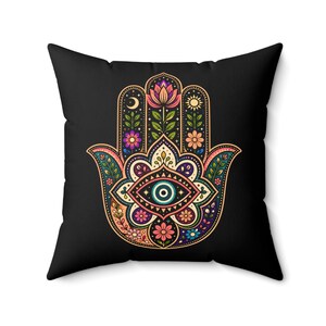 May include: Black square throw pillow featuring a colorful Hamsa hand design. The hand is decorated with an eye, flowers, a crescent moon, and a sun. The design incorporates pink, blue, green, orange, and purple hues.
