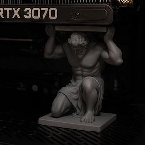 May include: A gray statue of a kneeling Atlas figure supporting a black RTX 3070 graphics card. The statue is on a square base. The graphics card has the text "RTX 3070" in white.