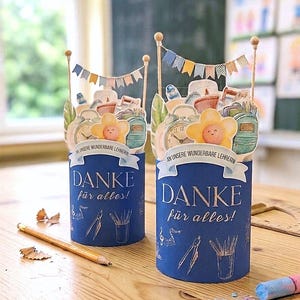 Könnte beinhalten: Zwei zylindrische blaue Papierbehälter mit dem Text "DANKE für alles!" und "AN UNSERE WUNDERBARE LEHRERIN". Die Oberseiten sind mit Papieraufstellern von Schulutensilien, einer Uhr, einer Blume und einer kleinen Wimpelkette verziert.