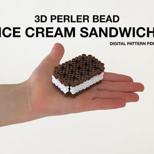 May include: A 3D Perler bead ice cream sandwich, held in a hand. The sandwich has a brown top and bottom with white filling. Text above reads "3D PERLER BEAD ICE CREAM SANDWICH" and "DIGITAL PATTERN PDF".