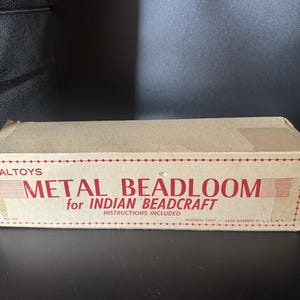May include: A rectangular cardboard box for a Waltoys Metal Beadloom for Indian Beadcraft. The box is tan with red text that reads Metal Beadloom for Indian Beadcraft, Instructions Included, No. 100, and Waltoys Corp. 44-02 Eleventh St. L.I.C. N.Y.