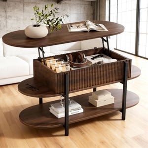 May include: A dark brown oval lift-top coffee table with a storage compartment. The table has two lower shelves and black metal legs. The top is open, revealing items inside the storage area, including headphones and small boxes. A white vase with greenery sits on top.