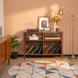 May include: A dark wood media console with two open shelves, featuring a record player on top, a framed floral print, a desk calendar showing 16, and a glass vase with orange flowers. The lower shelves hold vinyl records in metal dividers.