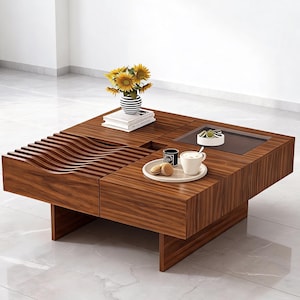 May include: A modern, square wooden coffee table with a rich brown finish. The table features a unique wave-like design on one side and a recessed glass-topped section. A vase of sunflowers, books, and a tray with coffee and cookies are on the table.