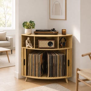 May include: A light oak corner media console featuring a top surface holding a record player and a candle. The middle shelf contains a radio, a small figurine, and headphones. The bottom section has two sliding doors housing vinyl records.
