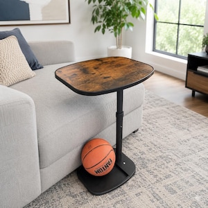 May include: A C-shaped side table with a dark brown wood-grain finish top and a black metal frame. The table features an adjustable height central post and a flat black base. An orange basketball with the word FANTOM is resting on the base.