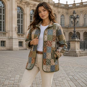 Puede incluir: Una chaqueta acolchada con un dise&ntilde;o de patchwork de varios patrones florales en tonos apagados de azul, verde, marr&oacute;n y crema. La chaqueta tiene un cuello redondo, mangas largas, cierre frontal de botones y ribetes de color verde oliva.