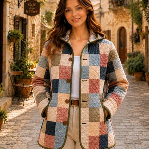 May include: A quilted jacket featuring a multi-colored patchwork pattern of squares in shades of blue, pink, and beige. The jacket has a hood, long sleeves, a front button closure with brown buttons, and olive green trim along the edges and pockets.