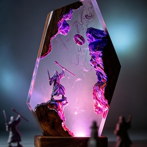 Può includere: Un'opera d'arte in resina a tema fantasy con una statuina di mago con un bastone e una spada. L'opera è racchiusa in una resina trasparente con accenti viola e rosa, all'interno di una cornice di legno. Il pezzo è illuminato da una luce soffusa e brillante.