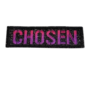 Peut inclure: Un écusson rectangulaire avec le mot "CHOSEN" en lettres violettes et roses dégradées. Les lettres sont soulignées d'une teinte plus foncée, et le fond est noir avec des paillettes.