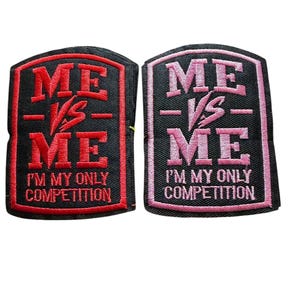 May include: Two rectangular embroidered patches with black backgrounds. One features red text and border, the other pink. Both display the text ME VS ME and I'M MY ONLY COMPETITION in a bold, block-style font with a central VS graphic element.