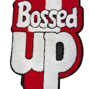 Può includere: Un tappeto rosso, bianco e nero con la scritta "Bossed Up" in un carattere audace e stilizzato. Le lettere sono bianche con un contorno nero, su uno sfondo a strisce rosse e bianche.