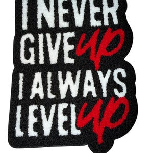 May include: Black rectangular mat with the words "I NEVER GIVE UP I ALWAYS LEVEL UP" in white and red. The mat has a textured surface and a unique shape.