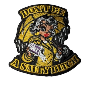 May include: Embroidered patch featuring a cartoon woman in a yellow raincoat and umbrella, with the text "DON'T BE A SALTY BITCH". The woman is holding a container of salt. The patch has a black border and yellow and white accents.