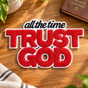 May include: A punch needle wall hanging featuring the black text all the time above the red, textured, punch needle letters spelling TRUST GOD. The letters are outlined in white, creating a bold, dimensional appearance on a flat surface.