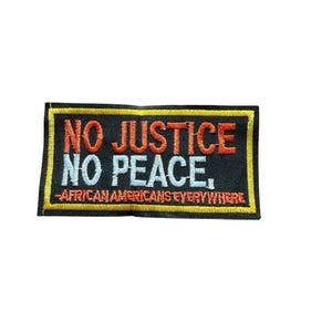 May include: A rectangular embroidered patch with a black background and a yellow border. The text NO JUSTICE is in orange, NO PEACE is in light blue, and AFRICAN AMERICANS EVERYWHERE is in orange, all stitched in a bold, sans-serif font.