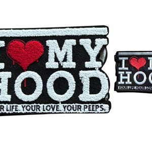 Peut inclure: Deux écussons brodés noirs et blancs. Le plus grand porte l'inscription "I MY HOOD" avec un cœur rouge et le texte "YOUR LIFE. YOUR LOVE. YOUR PEEPS." Le plus petit a le même design.