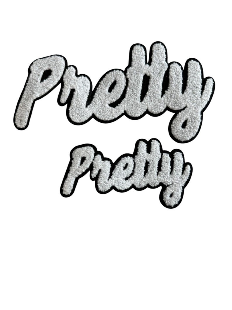 May include: Two white, fluffy "Pretty" patches with a black border. The word is written in a cursive, playful font. The patches are in two sizes, one large and one small, and are set against a white background.
