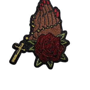 Peut inclure: Écusson brodé représentant des mains jointes en prière avec des ongles rouges, un chapelet, une rose rouge et une croix dorée. Le patch a une bordure noire avec des accents verts sur la rose.