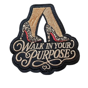May include: An embroidered patch featuring a pair of legs wearing leopard print high heels with red soles. Below the legs, the text "WALK IN YOUR PURPOSE" is stitched in gold thread with a decorative flourish and a small heart at the bottom.