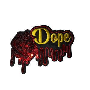 May include: Embroidered patch with the word "Dope" in yellow script, outlined in black, on a black background with red dripping accents. A red sequined design is on the left side.