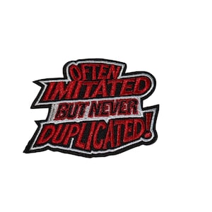 May include: Embroidered patch with the words "Often Imitated But Never Duplicated!" in red, outlined in black and white. The patch has a unique, stylized shape, perfect for adding to clothing or accessories.