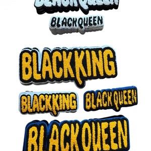 Può includere: Una collezione di toppe ricamate con le frasi "BLACK QUEEN" e "BLACK KING". Le toppe presentano testo giallo con bordi neri e blu. Le toppe sono progettate con un aspetto strutturato e in rilievo.