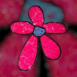 Puede incluir: Primer plano de una flor decorativa con cinco p&eacute;talos de color rosa brillante, cada uno cubierto de lentejuelas. El centro es azul con un patr&oacute;n de puntos y los bordes est&aacute;n delineados en negro.