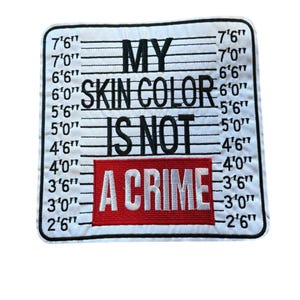May include: A rectangular embroidered patch with a white background featuring a black police mugshot height chart. The text reads MY SKIN COLOR IS NOT A CRIME, with the words A CRIME displayed in white letters inside a solid red rectangular block.