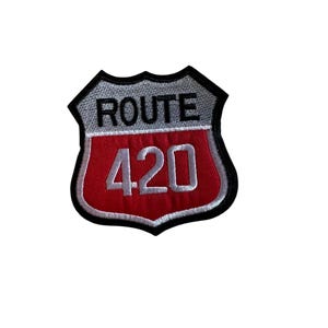 Puede incluir: Un parche de la Ruta 420 con forma de escudo. El parche tiene un borde negro, una sección superior gris con la palabra "ROUTE" en blanco y una sección inferior roja con el número "420" en blanco.
