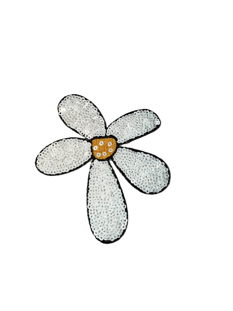 Puede incluir: Aplicaci&oacute;n en forma de margarita blanca con ribete negro. Los p&eacute;talos est&aacute;n cubiertos de lentejuelas blancas y el centro es de color dorado texturizado. Esta aplicaci&oacute;n decorativa se puede coser en ropa o accesorios.