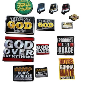 May include: A collection of embroidered patches with religious and inspirational themes. The patches feature phrases like "Trust God," "God Over Everything," and "Product of Grace." Colors include black, gold, red, and white. Some patches have text from the Bible.