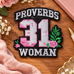 May include: A black embroidered patch featuring the white text PROVERBS at the top and WOMAN at the bottom. The centre displays the large number 31 in silver and pink thread, accented by a green leafy branch and a small pink rose on the right side.