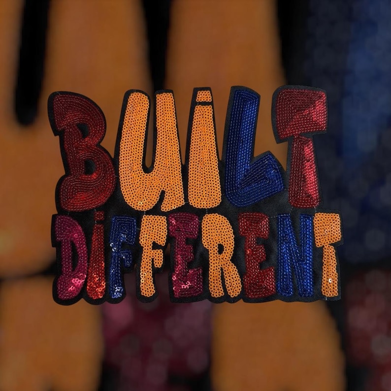 以下が含まれることがあります： カラフルなスパンコールで刺繍された「BUILT DIFFERENT」の文字が入った黒いパッチ。文字はオレンジ、赤、青、ピンク。衣類やアクセサリー用のパッチです。