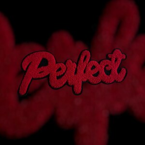 May include: Red embroidered patch with the word "Perfect" in a cursive font. The patch has a black border and a textured, fuzzy appearance. The background is a blurred red color, with a black backdrop.