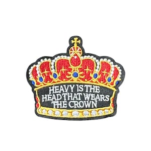 May include: Embroidered patch featuring a red and gold crown design with blue and white accents. The patch has the text "HEAVY IS THE HEAD THAT WEARS THE CROWN" in white letters on a black background. The patch is likely for clothing or accessories.