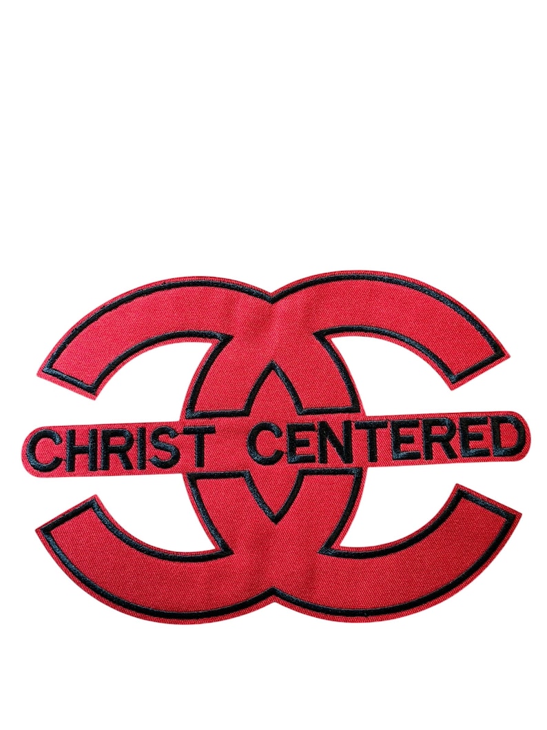 Puede incluir: Un parche bordado de color rojo con un dise&ntilde;o circular entrelazado estilizado y contorno negro. El texto CHRIST CENTERED est&aacute; bordado en letras may&uacute;sculas negras en el centro del dise&ntilde;o, dividiendo horizontalmente las dos formas entrelazadas.