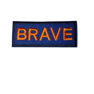 Peut inclure: Un écusson rectangulaire bleu avec le mot "BRAVE" brodé en orange. Le patch est bordé de noir, conçu pour être cousu sur des vêtements ou des accessoires.