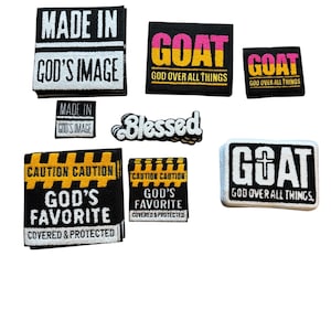 Könnte beinhalten: Eine Sammlung von gestickten Aufnähern mit verschiedenen Designs und Texten. Die Aufnäher zeigen Sätze wie "MADE IN GOD'S IMAGE", "GOAT GOD OVER ALL THINGS" und "GOD'S FAVORITE COVERED & PROTECTED". Farben sind Schwarz, Weiß, Gelb, Rosa und Blau.