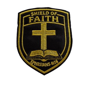 Könnte beinhalten: Schwarz-goldener, gestickter Aufnäher in Schildform. Der Aufnäher zeigt den Text "SHIELD OF FAITH", ein goldenes Kreuz und ein offenes Buch. Der Text "EPHESIANS 6:16" befindet sich unten. Geeignet für Kleidung oder Accessoires.