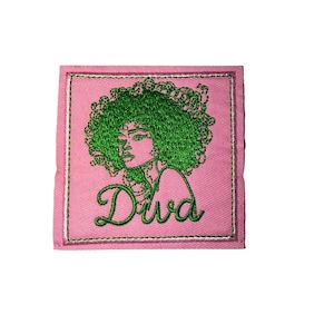 May include: Pink embroidered patch featuring a green-haired woman with the word "Diva" in cursive. The patch has a pink background with a green border, creating a vibrant and eye-catching design. The embroidery is detailed and the overall aesthetic is stylish.