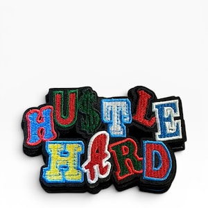 May include: An embroidered patch featuring the words HUSTLE HARD in a multi-colored block letter style. The letters are outlined in black and filled with various colors including red, green, blue, and yellow, set against a black background.