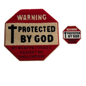 Puede incluir: Dos parches rojos y beige con el texto "WARNING PROTECTED BY GOD" y una cruz. El parche más grande también incluye el texto "NO WEAPON FORMED AGAINST ME SHALL PROSPER". Los parches son octogonales.