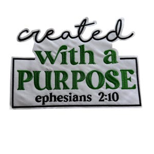 Pode incluir: Patch bordado com as palavras "created" em escrita preta sobre um retângulo branco. O retângulo apresenta o texto "With a PURPOSE" em verde e "ephesians 2:10" em verde.