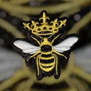 Peut inclure: Écusson brodé d'une abeille noire, dorée et blanche, ornée d'une couronne dorée. L'abeille a des ailes blanches, un corps noir avec des rayures dorées et des contours dorés. La couronne est dorée avec des détails complexes. Pour vêtements ou accessoires.