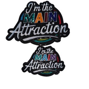 May include: Two black patches with the text "I'm the MAIN Attraction". The word "MAIN" is in colorful sequins. The patches have a black beaded border and white embroidered text.