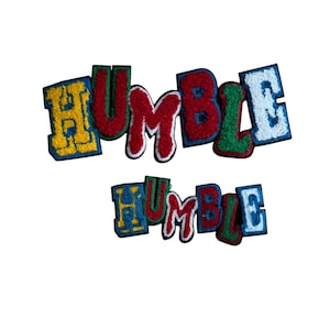 Può includere: Due toppe ricamate con la scritta "HUMBLE" in lettere colorate in stile college. La toppa superiore è più grande, con lettere gialle, rosse, verdi e blu. La toppa inferiore è una versione più piccola dello stesso design.